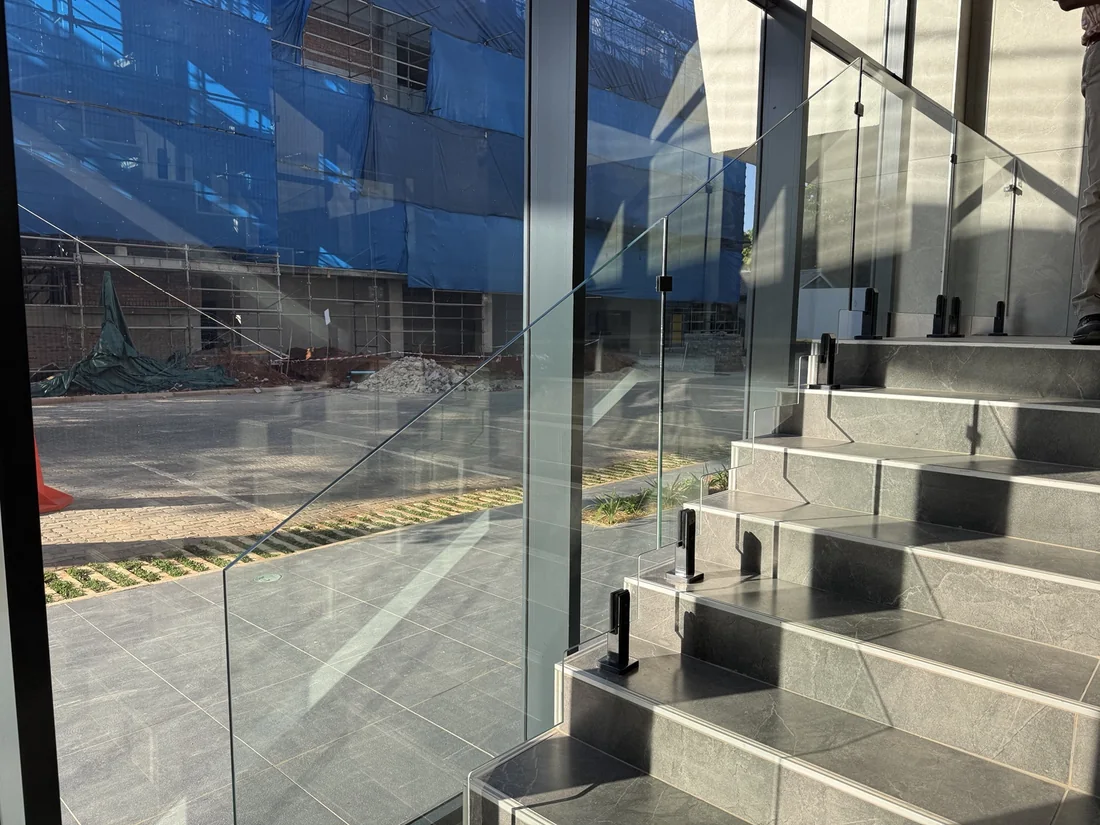 Glass balustrade on a tiled staircase with dark metal clamps, in Kingson Engineering’s supplied project photograph.