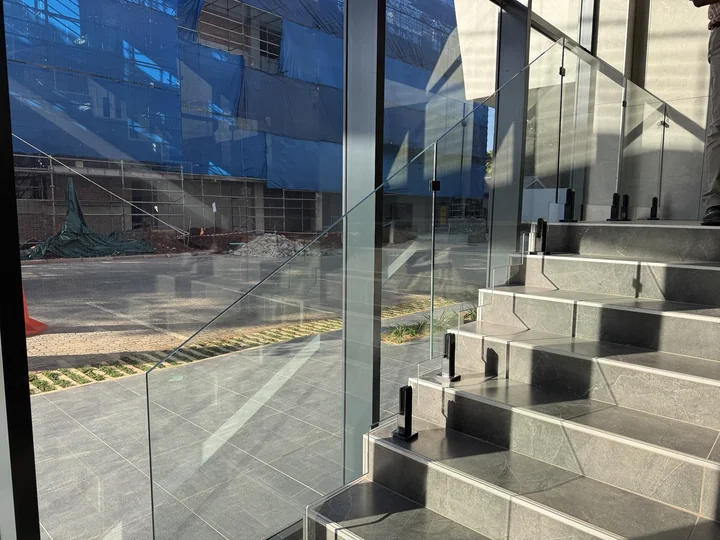 Glass balustrade on a tiled staircase with dark metal clamps, in Kingson Engineering’s supplied project photograph.