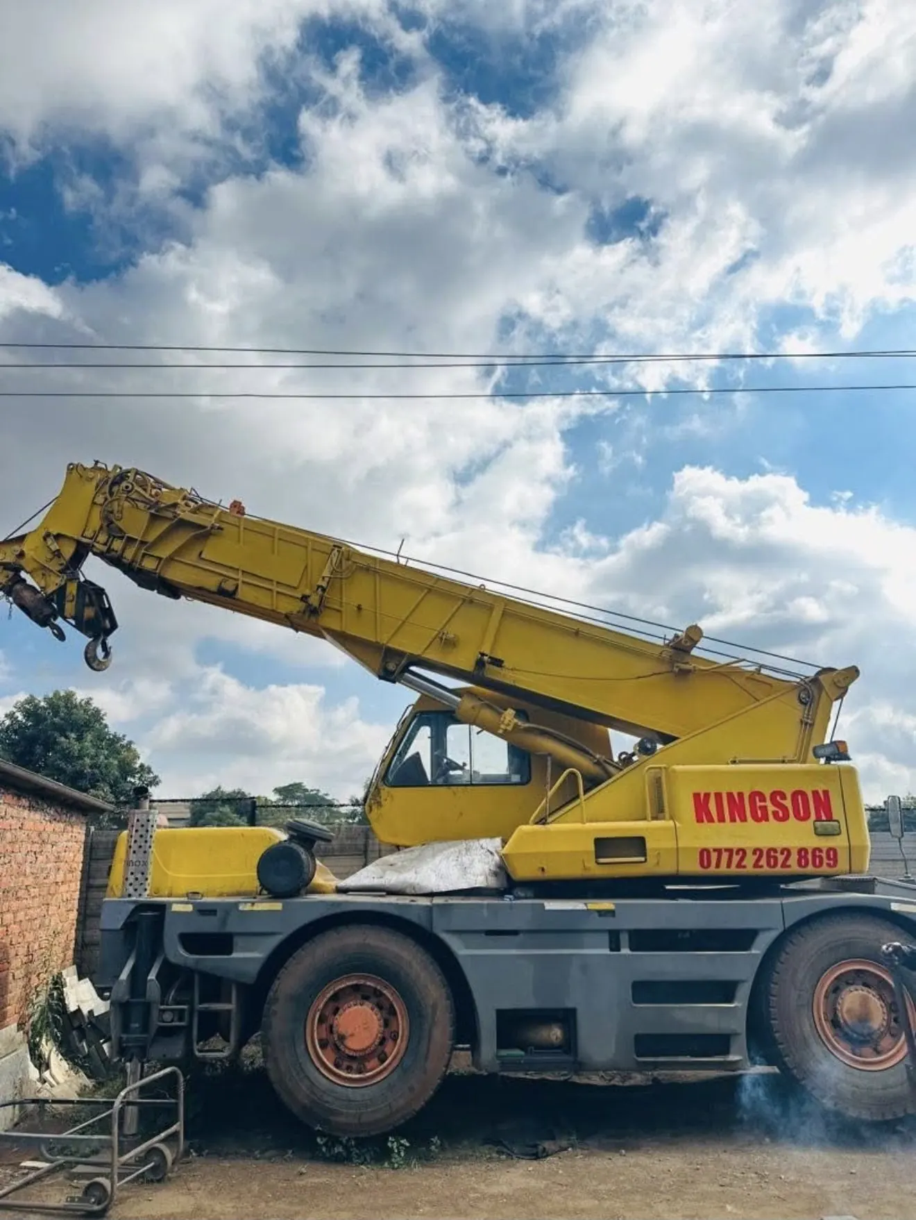 A yellow telescopic mobile crane standing in a yard, boom raised, with lettering reading KINGSON and a phone number on the counterweight body.