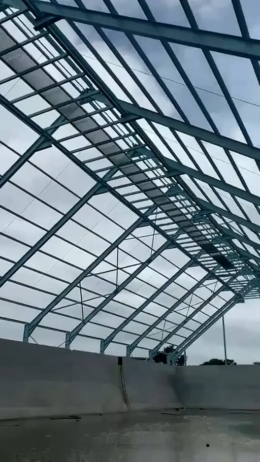 Blue-painted Kingson roof members and purlins receding beneath partial sheeting, with open bays against the sky.
